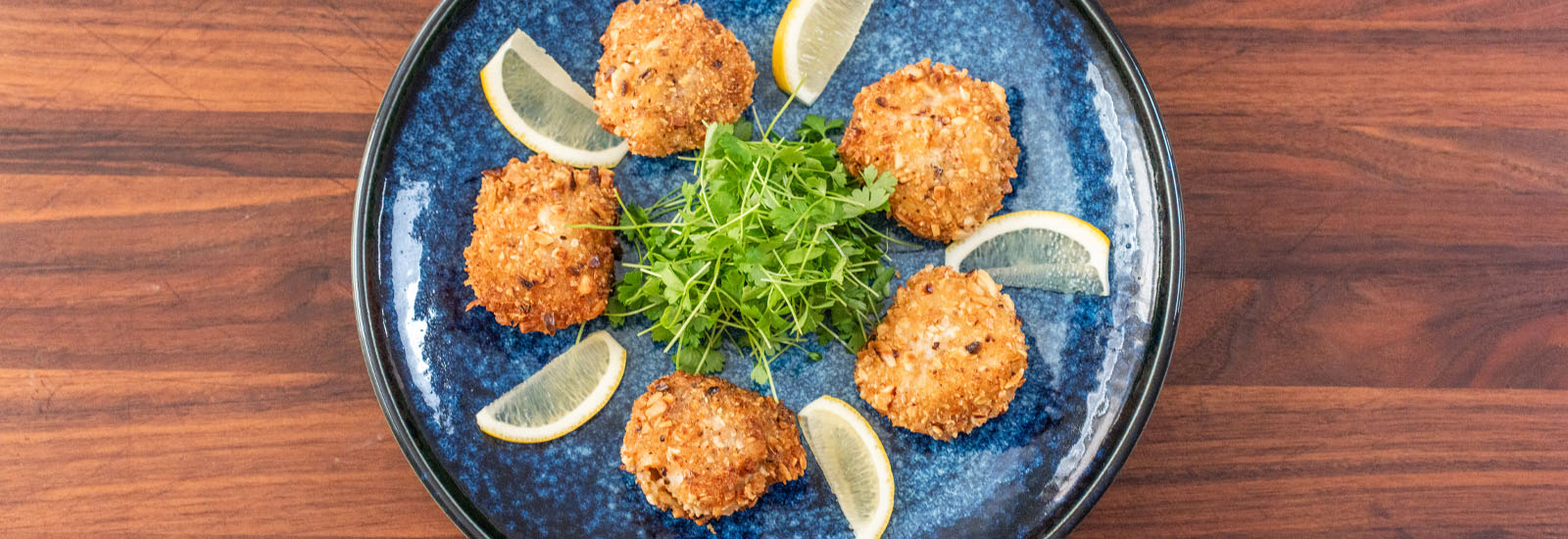 Plated almond panko crusted Lighthouse Seafoods sea scallops with lemon wedges and greens seafood appetizer.