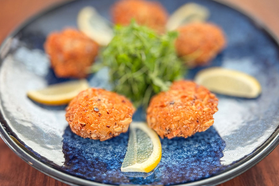 Plated almond panko crusted Lighthouse Seafoods sea scallops with lemon wedges and greens seafood appetizer.