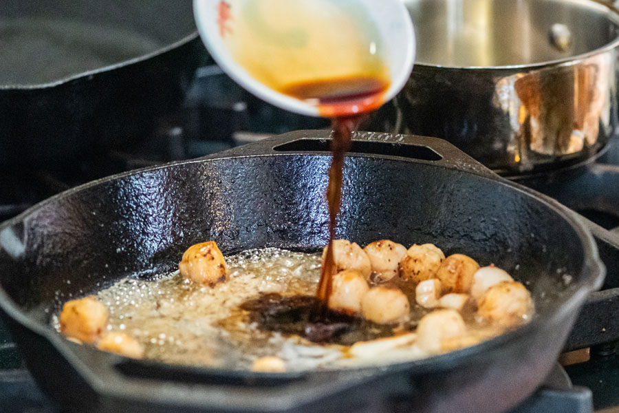 Chef pouring sauce over seared bay scallops in a cast iron skillet for Lighthouse Seafoods recipe.