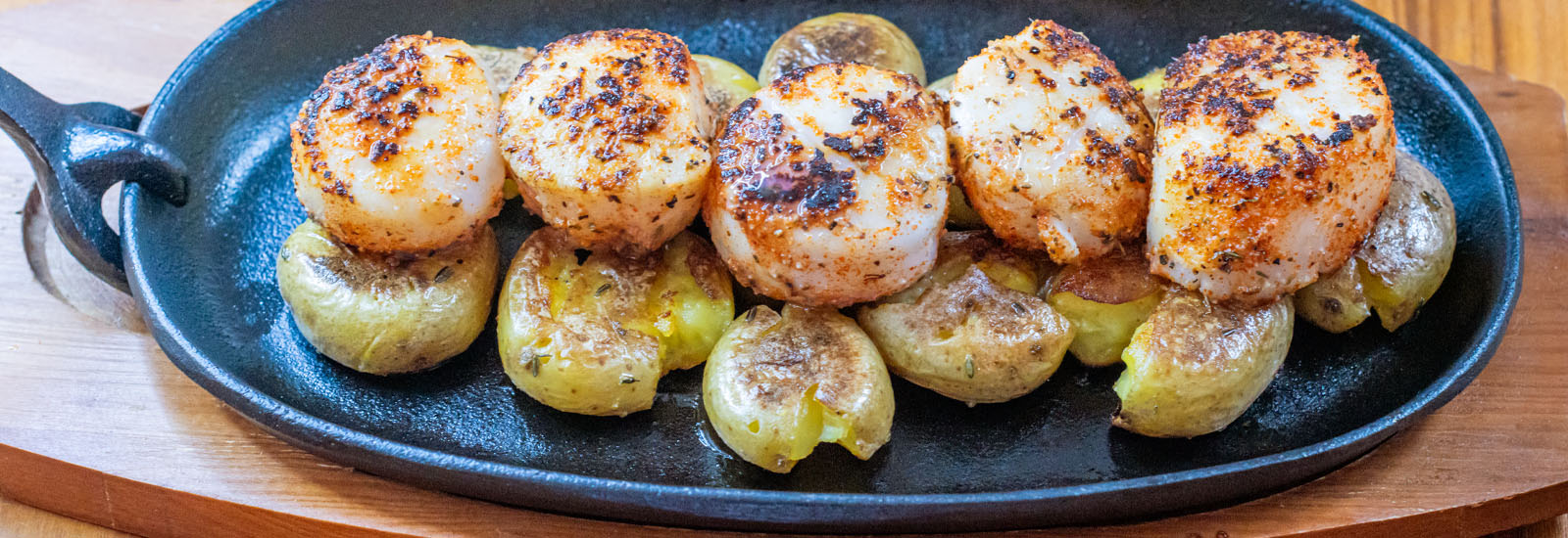Plated seared Lighthouse Seafoods sea scallops with crispy smashed potatoes and fresh lemon.