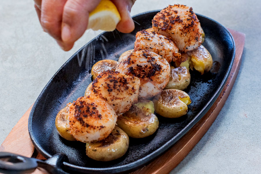 Plated seared Lighthouse Seafoods sea scallops with crispy smashed potatoes and fresh lemon.