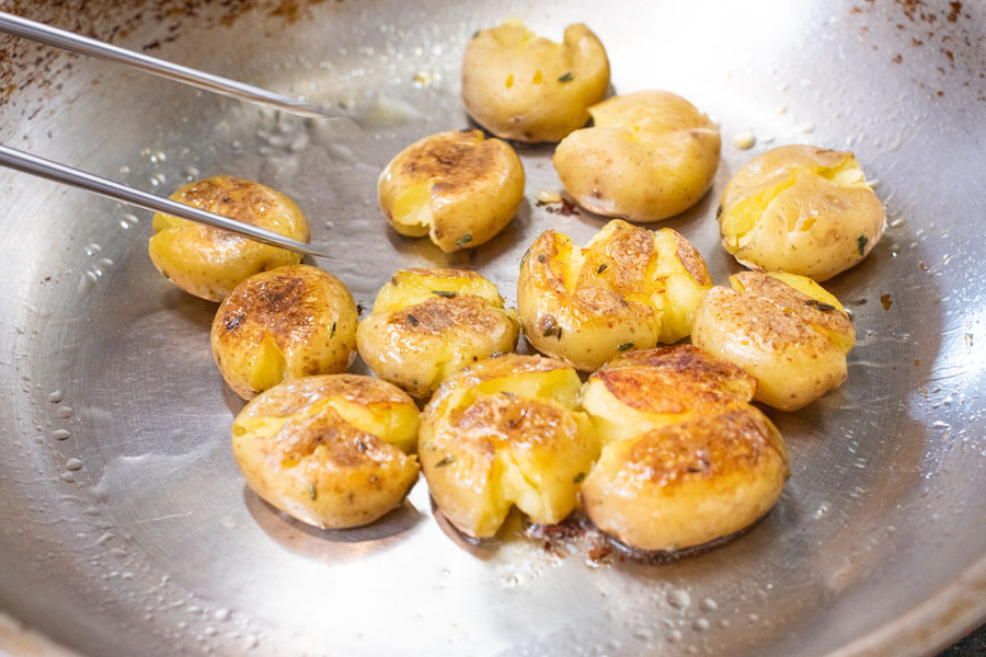 Sautéing crispy smashed baby potatoes in pan for Lighthouse Seafoods seared sea scallops with smashed potatoes recipe.